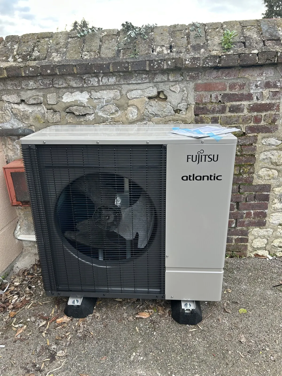 Pompe à chaleur air-eau Fujitsu Atlantic installée par FDHE contre un mur de pierre au Petit-Quevilly