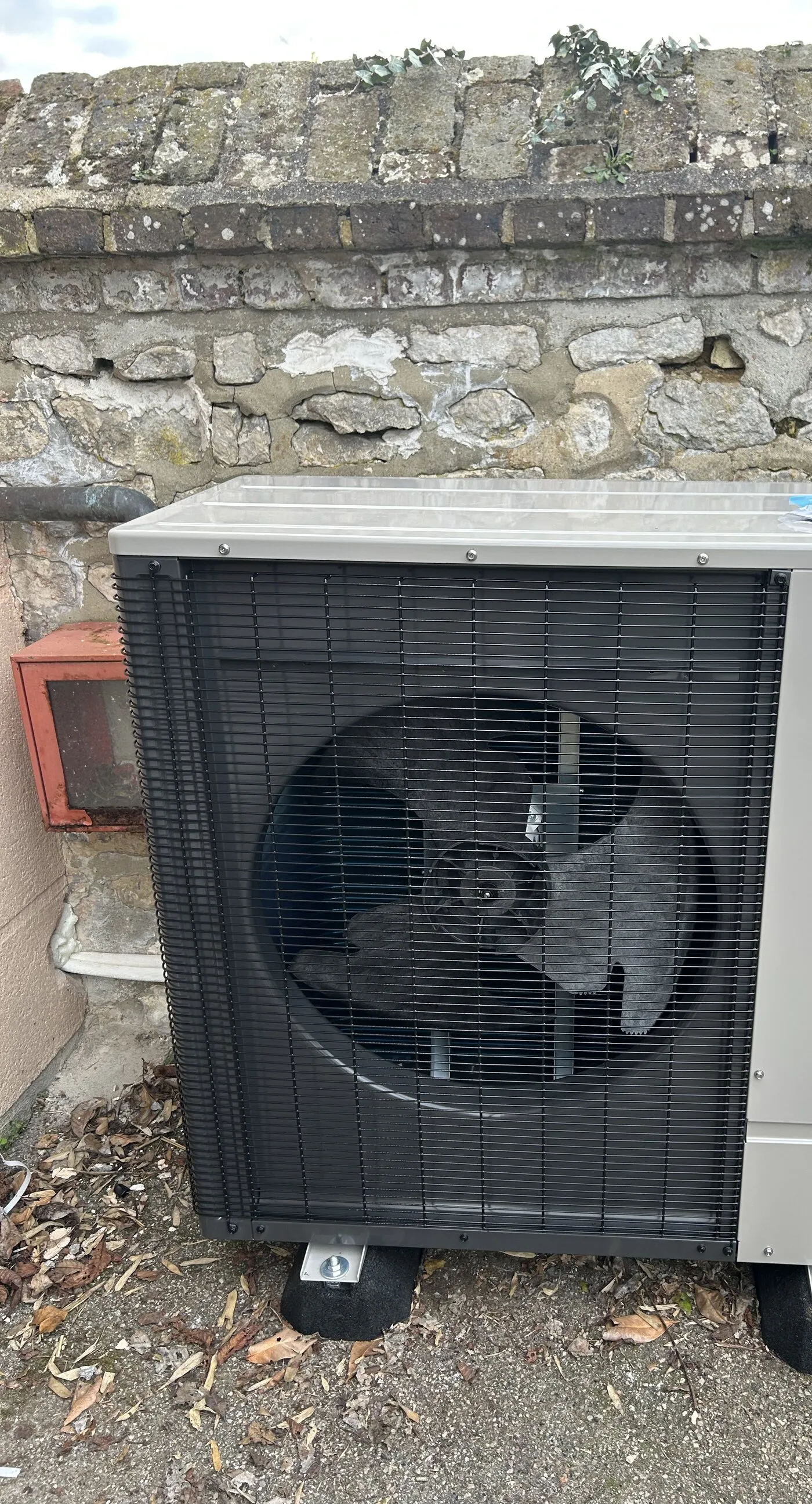 Pompe à chaleur air-eau installée par FDHE contre un mur de pierre au Petit-Quevilly